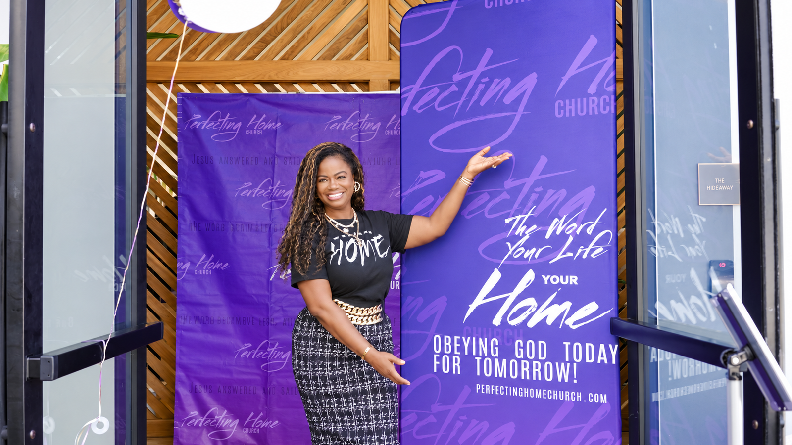 A woman welcomes visitors beside the Perfecting Home Church banner